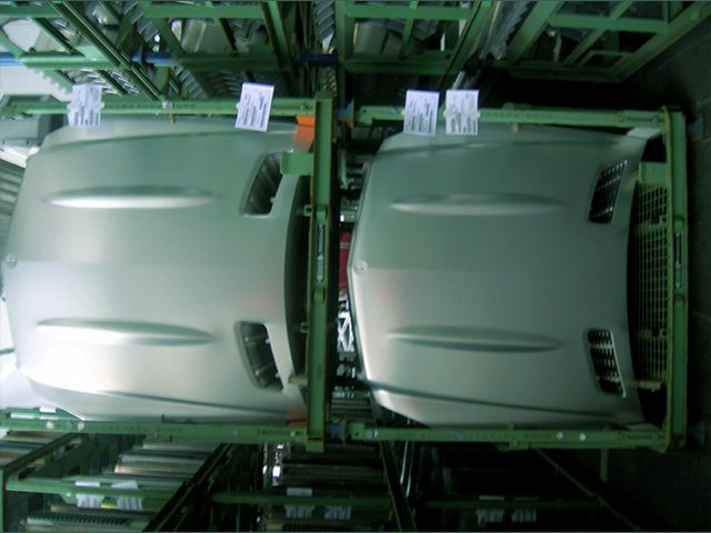 Silver automotive body panels mounted on an industrial rack during high-volume manufacturing ramp-up